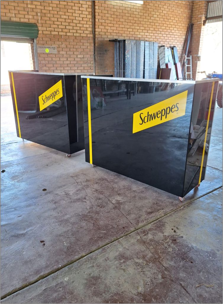 Custom-fabricated high-gloss Schweppes welcome counters with precision yellow branding, designed and manufactured by Specifusion for corporate hospitality and reception environments